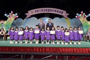 東華三院副主席李鋈麟博士太平紳士（後排右）陪同主禮嘉賓教育局副局長楊潤雄太平紳士（後排左）頒發畢業證書予幼稚園畢業學生代表。