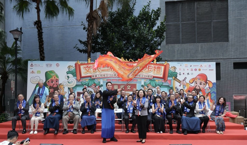 圖二為東華三院主席何猷啟先生（前排左）從民政及青年事務局局長麥美娟SBS太平紳士（前排右）手中接過出巡令旗，標誌著文武二帝出巡正式起步。